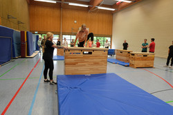 Eine Teilnehmerin springt im Parkour-Workshop über einen großen Kasten, während die Gruppe beobachtet
