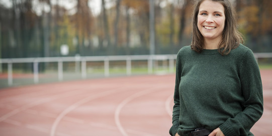 Lisa Muscular steht auf der Tartanbahn und lächelt in die Kamera. Sie ist bis knapp unterhalb der Hüfte zu sehen.
