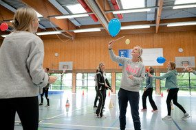Teilnehmer*innen halten im Workshop Harry Potter und der Stein der Weisen – Literacy und Bewegung in der Sporthalle einen Luftballon mit Hilfe eines Zauberstabs in der Luft