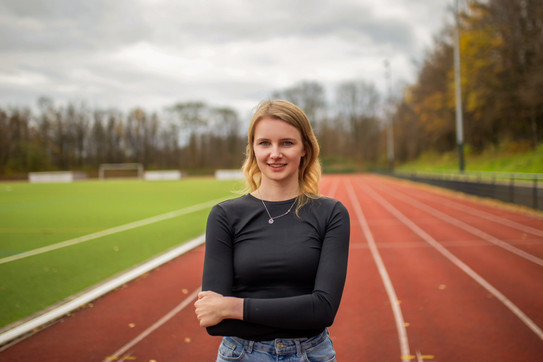 Annalena Veltmaat stands on the running track with her arms crossed and laughs into the camera.