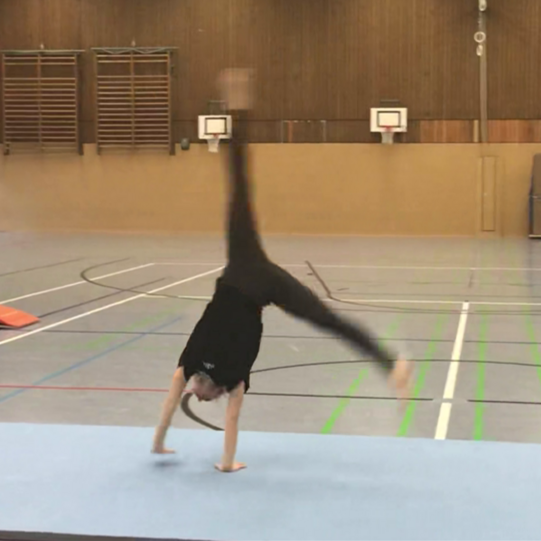Rad mit Angehen Eine Studierende schlägt ein Rad auf dem Bodenläufer