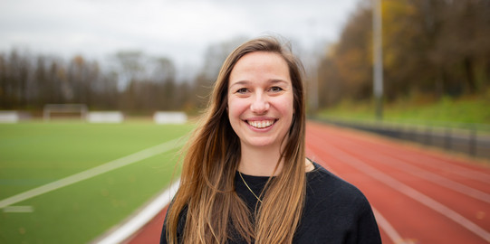 Dr. Charlotte Behlau steht auf der Tartanbahn und lacht in die Kamera.