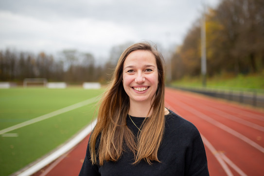 Dr. Charlotte Behlau steht auf der Tartanbahn und lacht in die Kamera.