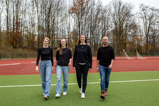 Das Team der Sportpsychologie ist auf dem Sportplatz und läuft lachend auf die Kamera zu. 